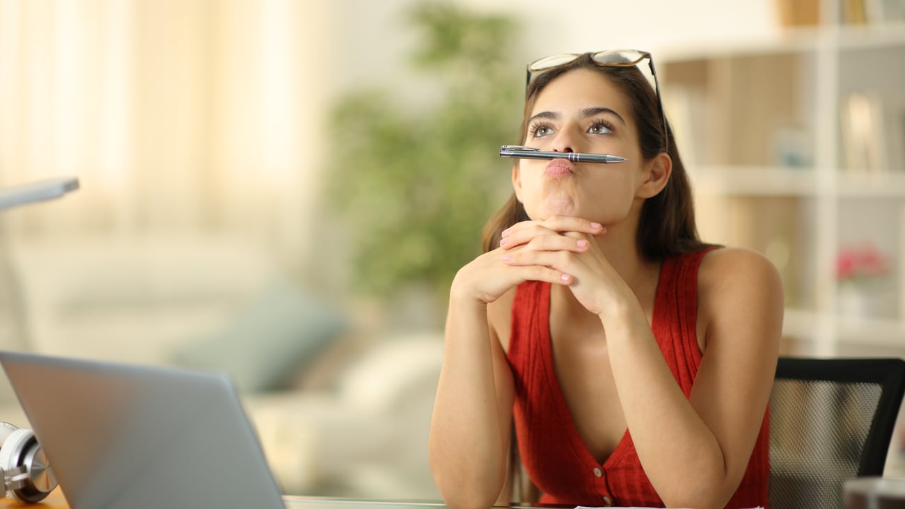 Young woman in front of computer, looking off, balancing pencil under her nose