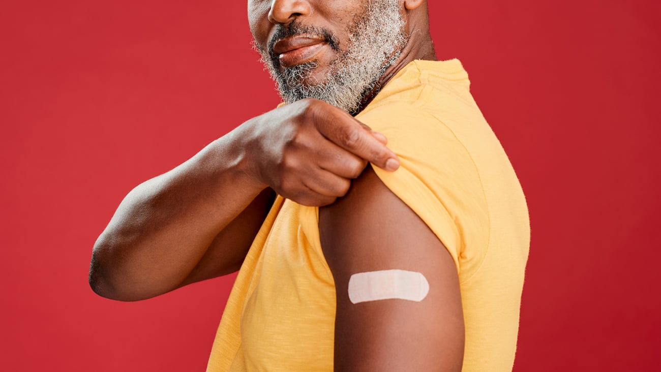 Middle-aged Black man holding up his yellow sleeve to show off a bandage where he received a vaccination