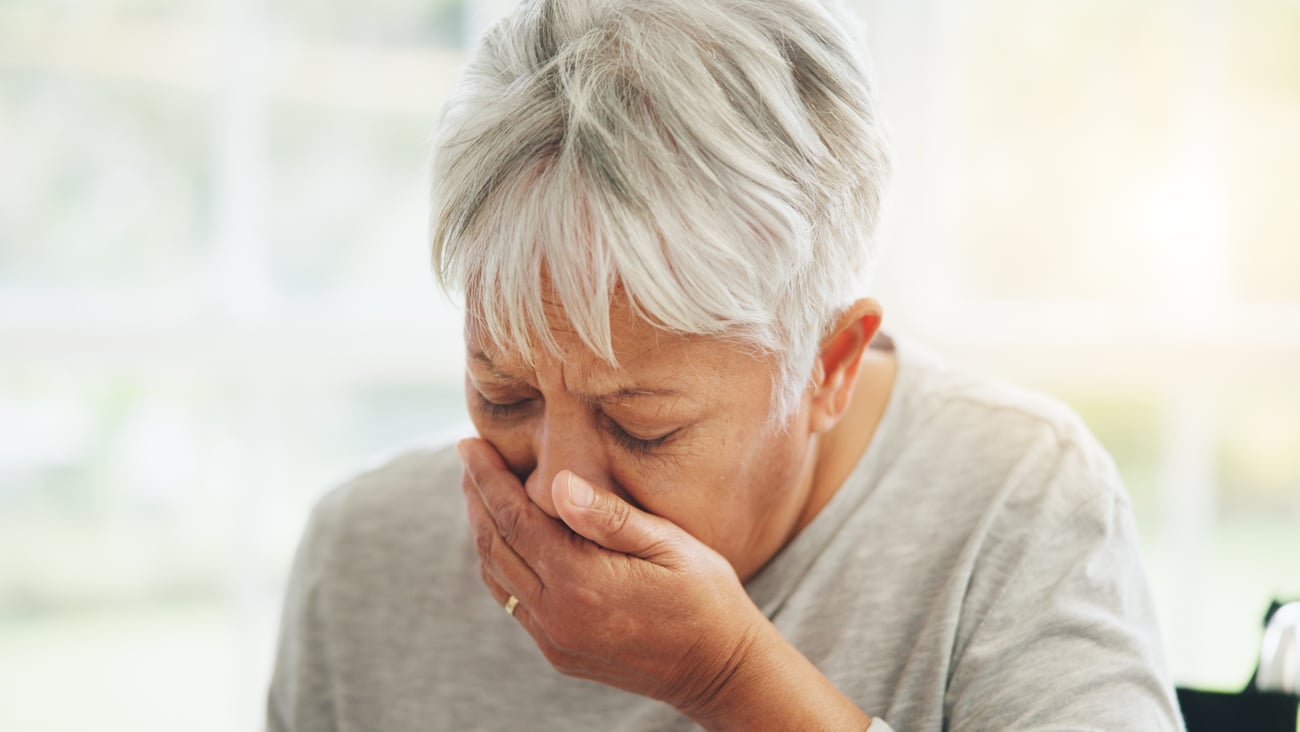 grey-haired woman with hand over mouth coughing