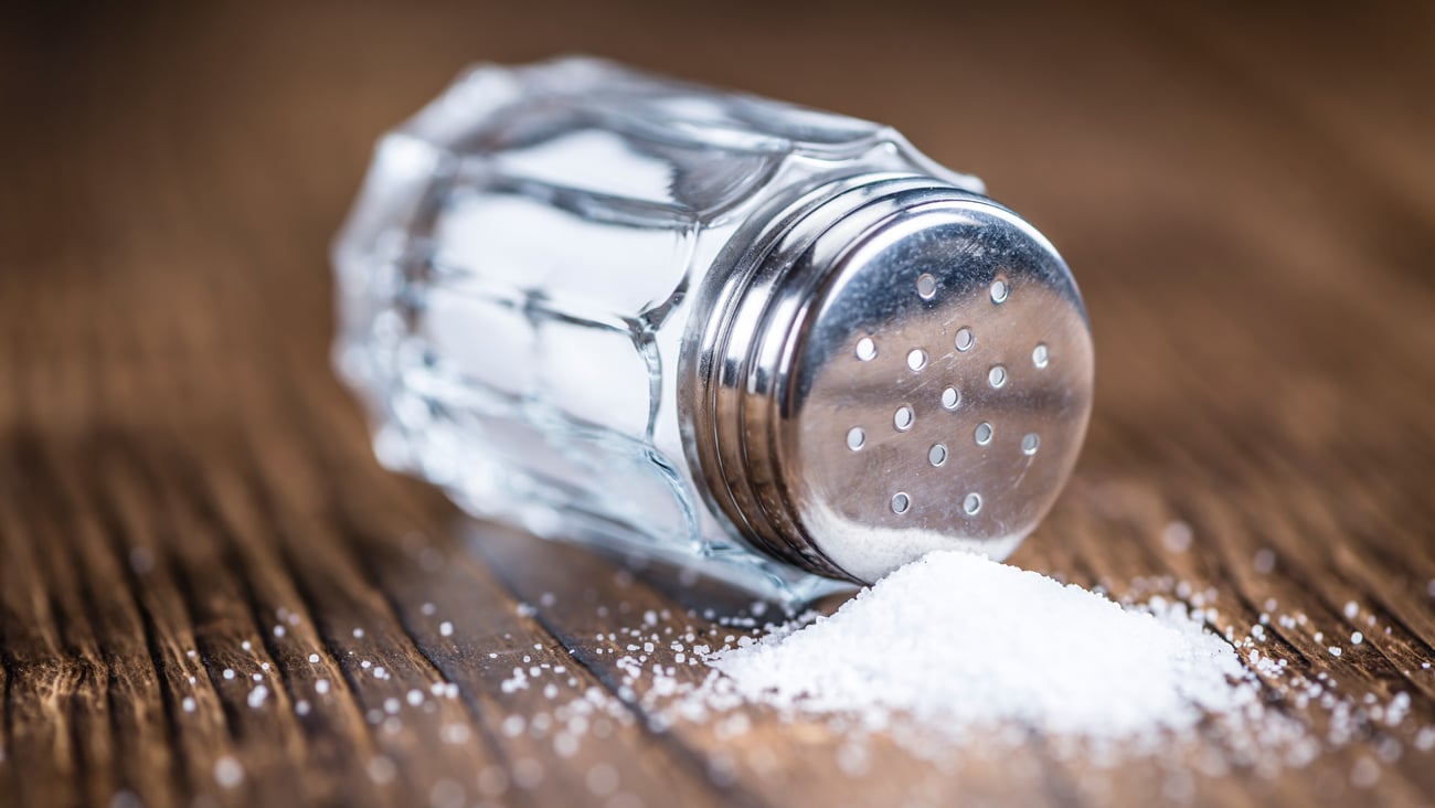 Small salt shaker spilled over on wooden table