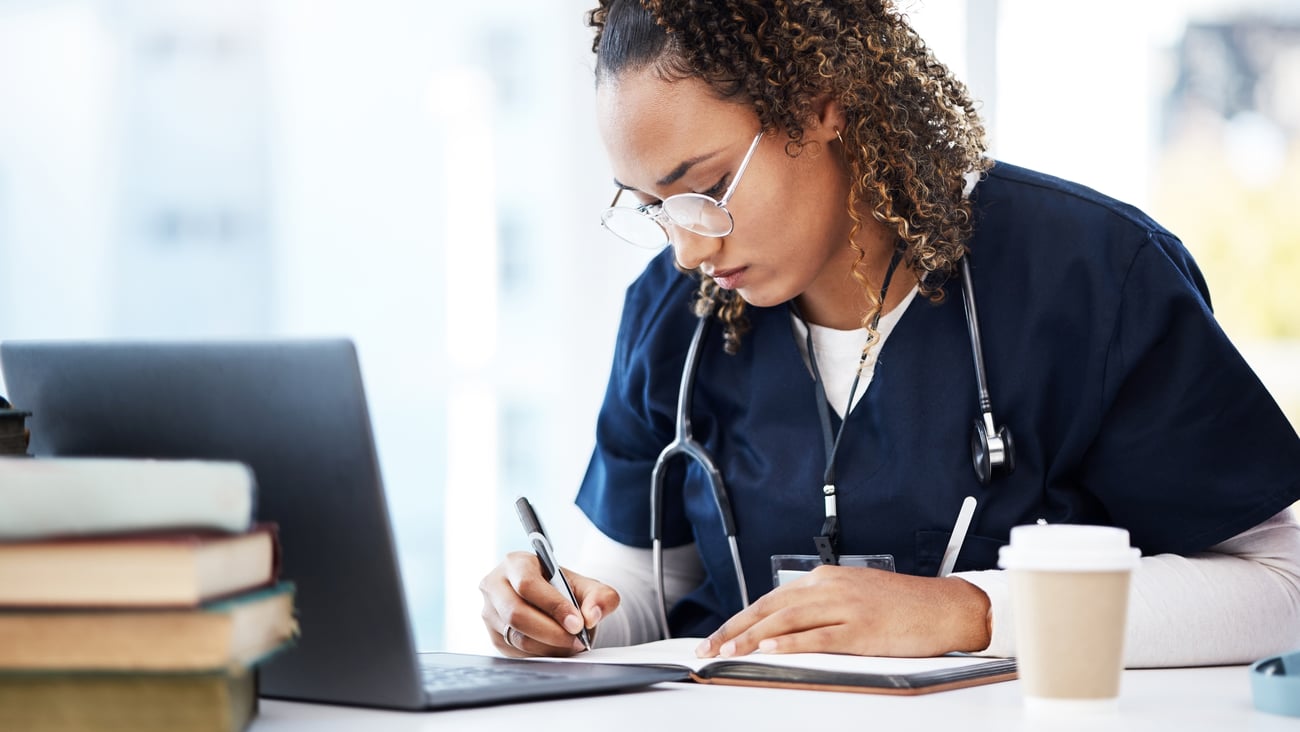 Young Black woman in blue scrubs reading medical textbooks