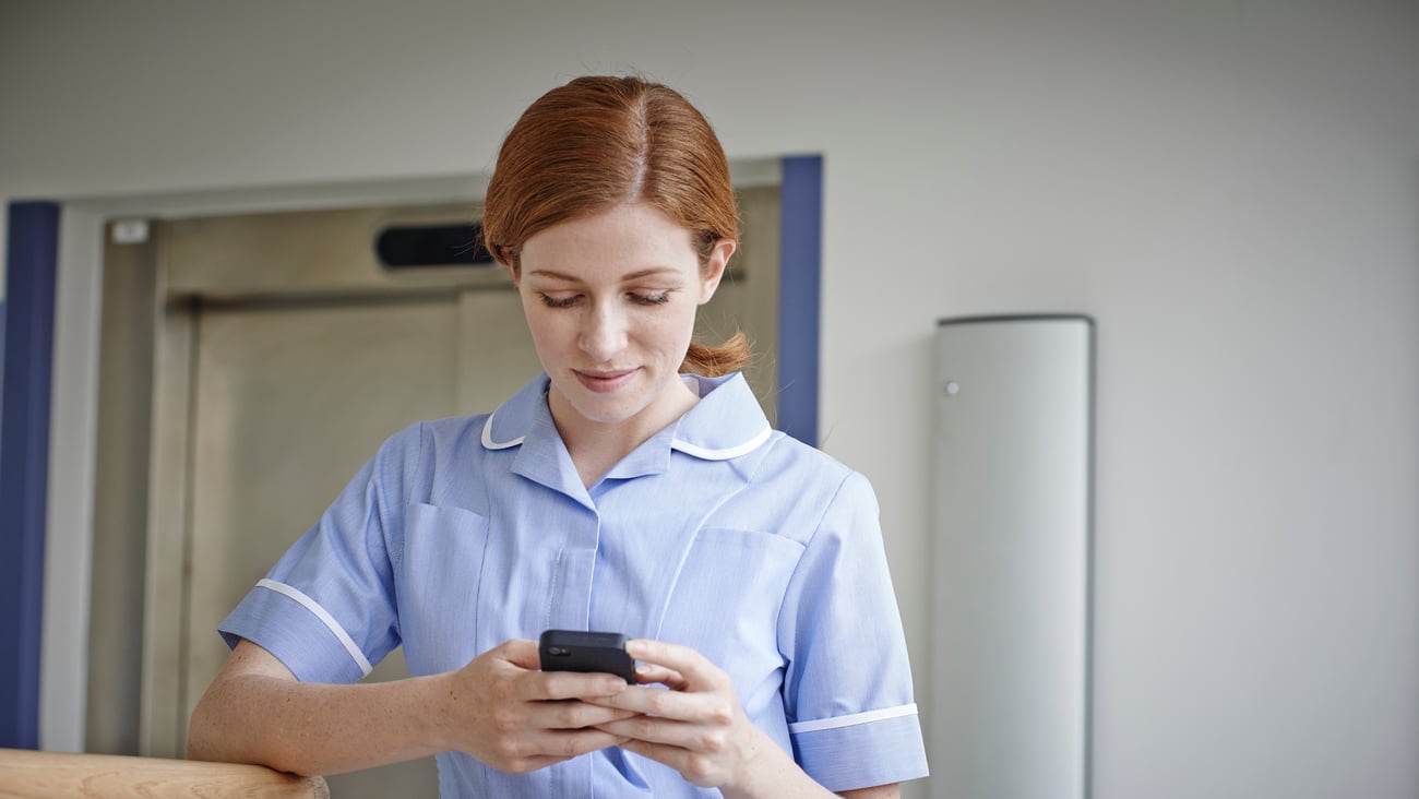 White young woman in nurse scrubs looking down at phone, slight smile