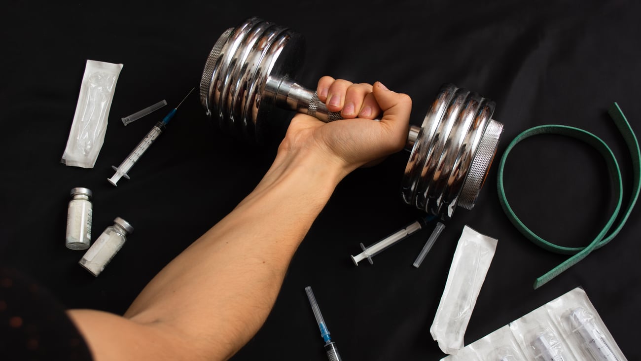 A man’s arm holding a dumbell, used syringes around him