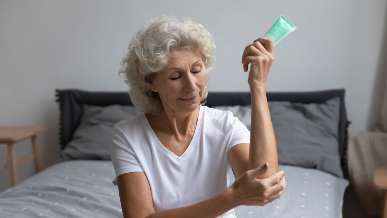 older woman applying moisturizer to elbow