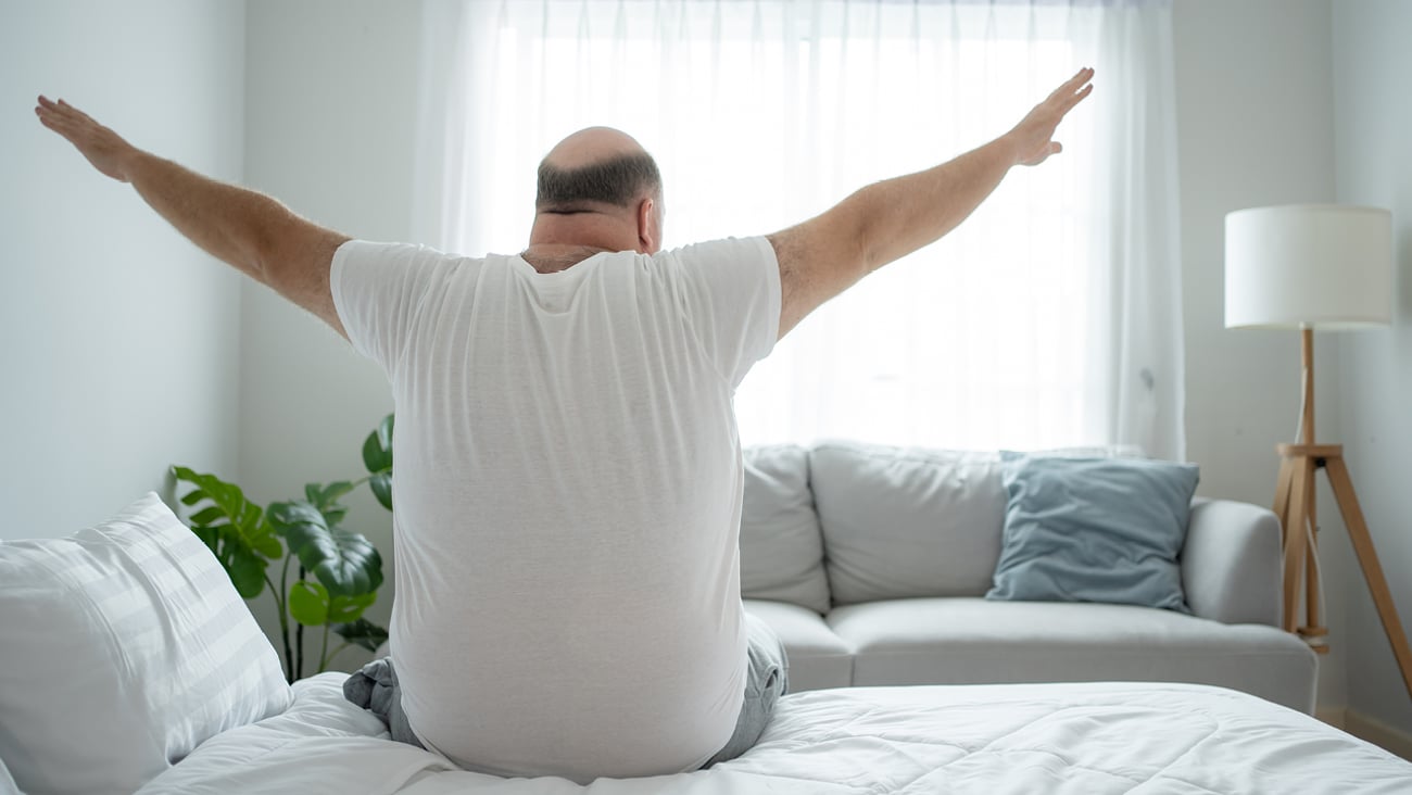 Larger middle-aged white man stretching in bed before starting his day