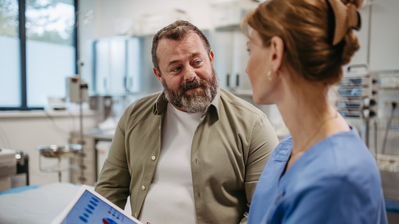 Female doctor consulting with overweight male patient holding tablet with diabetes test results