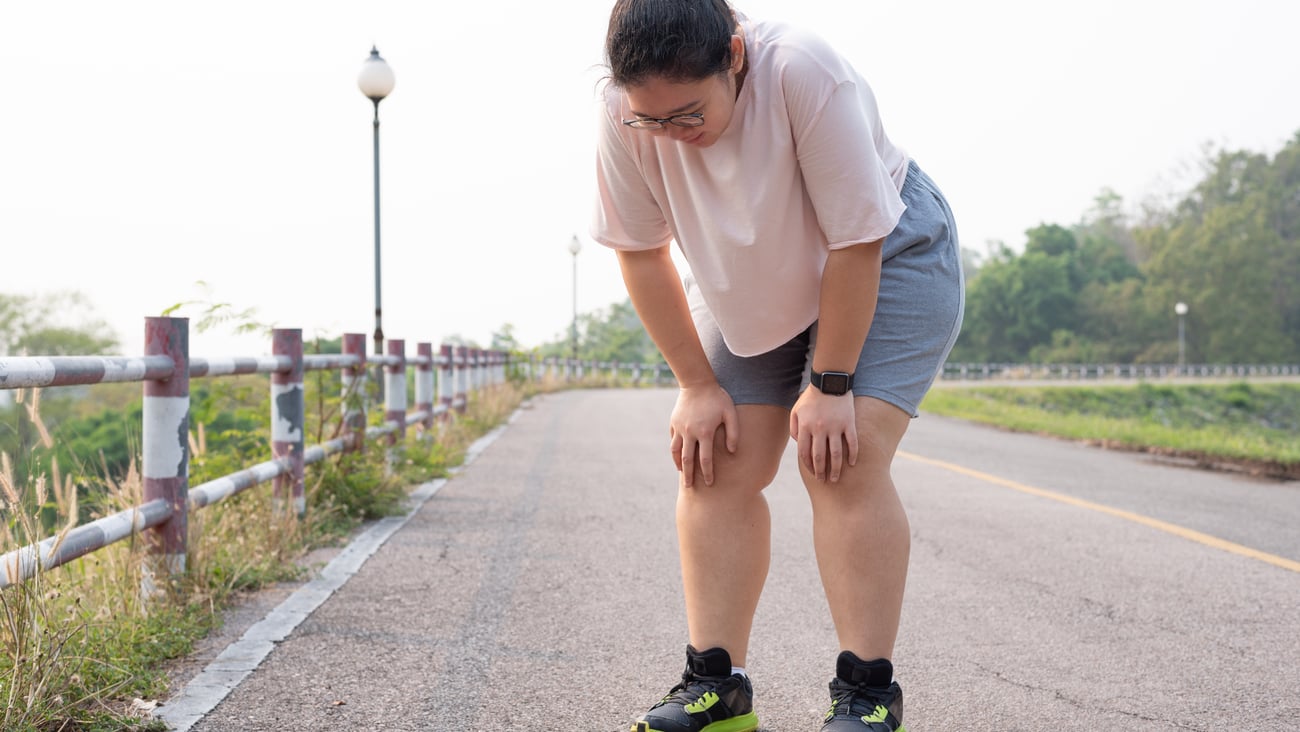 Asian woman bent over seemingly tired/out-of-breath while walking outside on a rural rolad