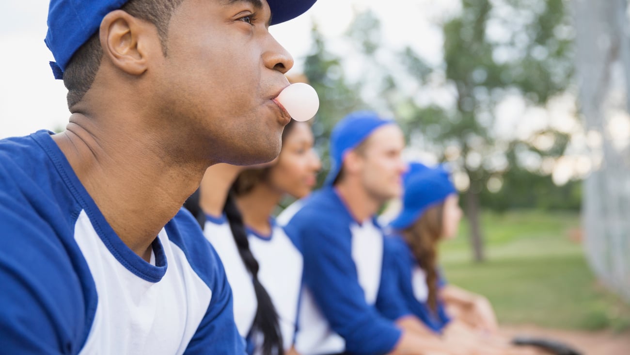 profile of people on team wearing blue and white jerseys and hats, man at front blowing a gum bubble.