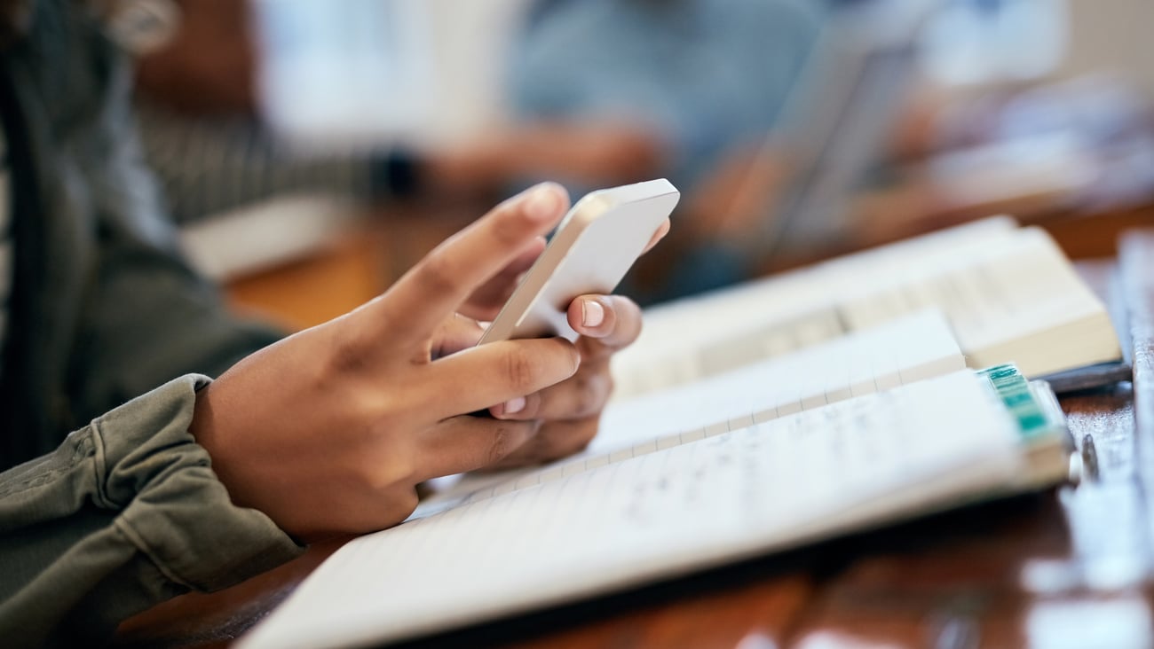 A person holding a cellphone is seen in a classroom.