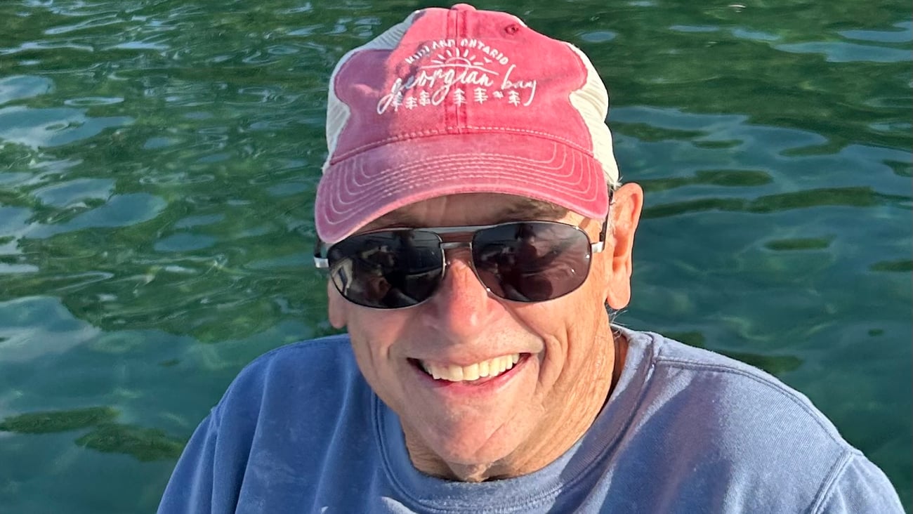 Dr, John Crosby in a red hat in front of a body of water