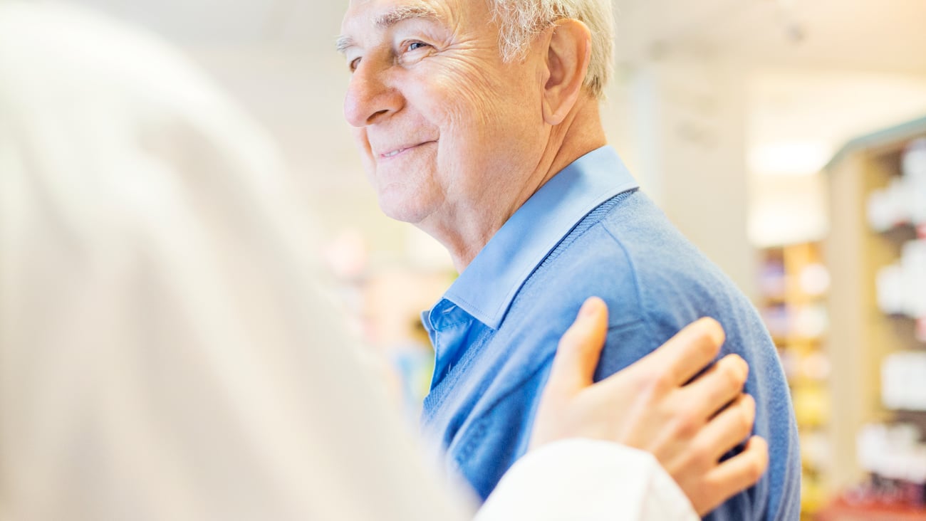 Elderly man being pat on the shoulder by pharmacist