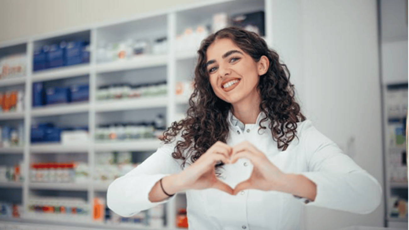 Young female pharmacist making heart hands symbol