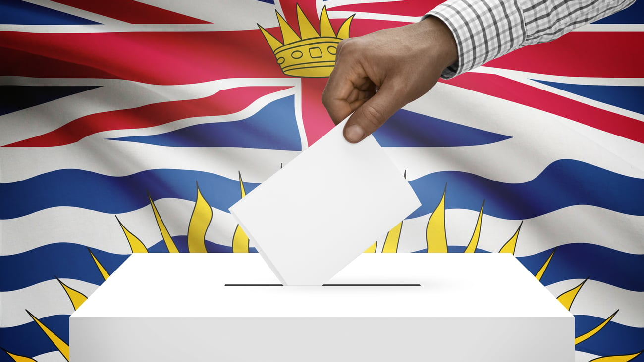 A ballot box with a hand is seen in front of the B.C. flag.