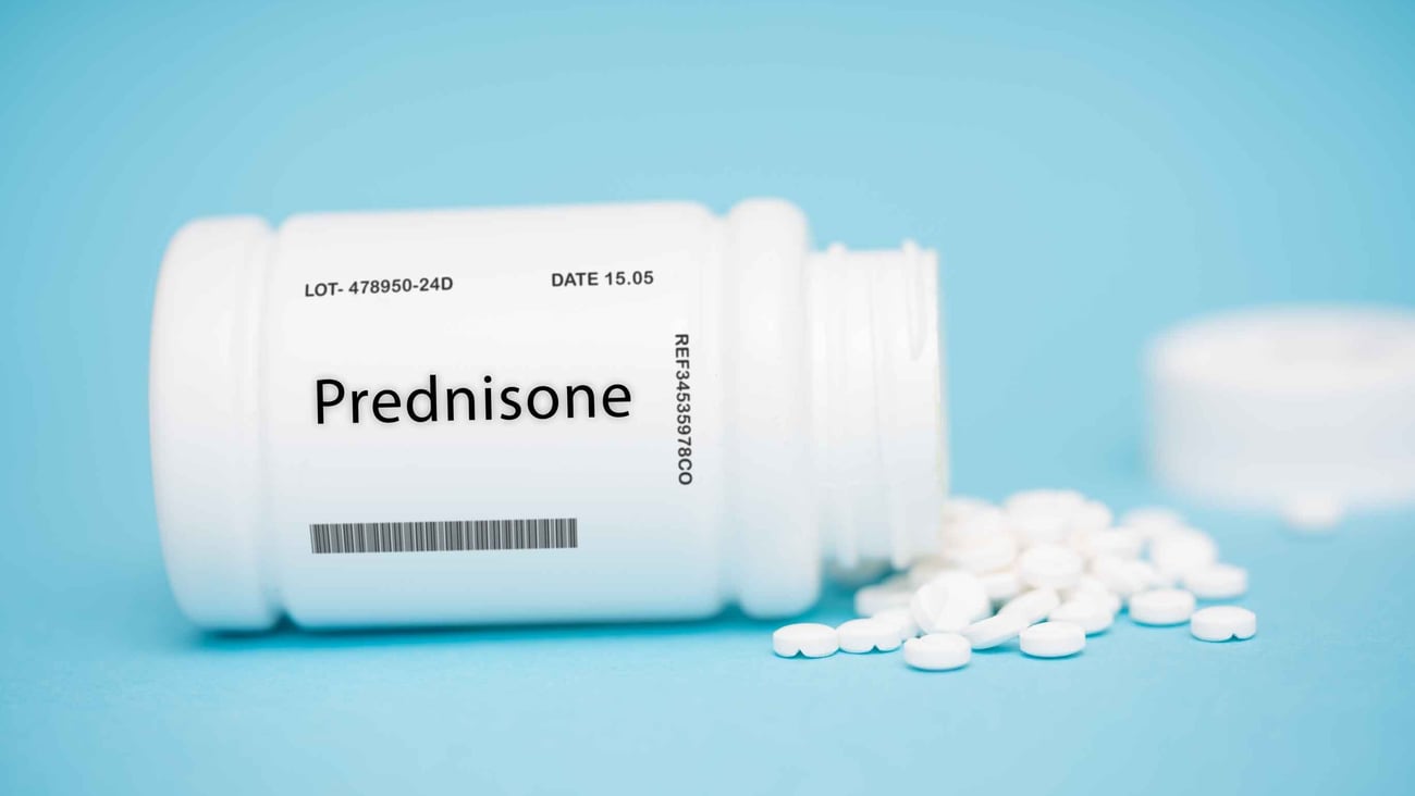 white bottle with word "prednisone" on it, sideways on blue background, white pills spilled out