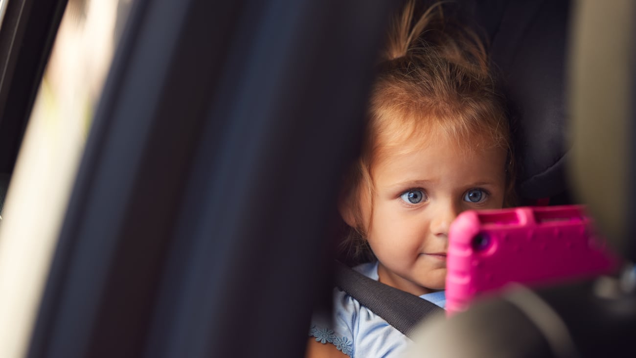 Little girl sitting in corner staring at pink tablet