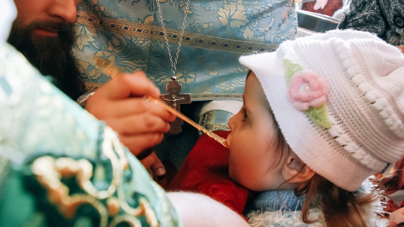 A child receives communion using a shared communion spoon at an Orthodox church.