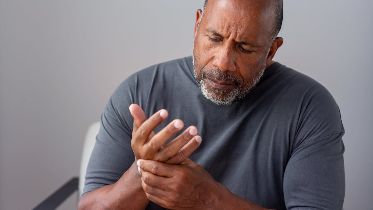 Older/middle-aged black man holding hand in pain.