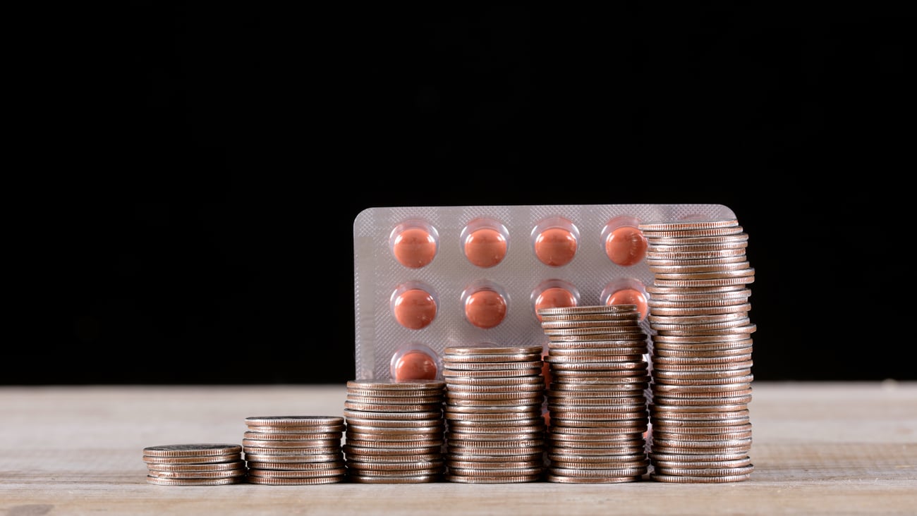 A stack of coins in front of a pack of pills