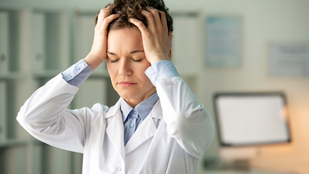 Young tired female chemist or pharmacist in whitecoat touching her head while standing in front of camera against workplace in laboratory; Shutterstock ID 1809842674