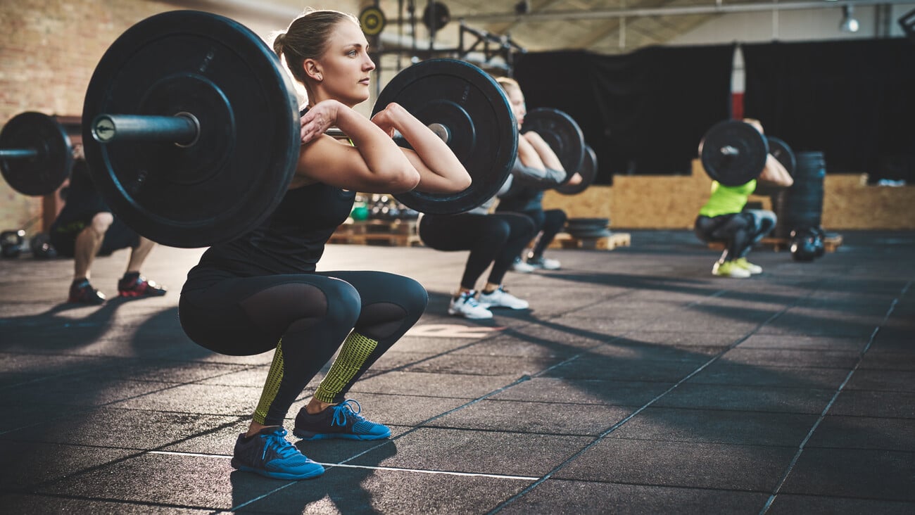 Fit young woman lifting barbells looking focused, working out in a gym with other people; Shutterstock ID 432200833