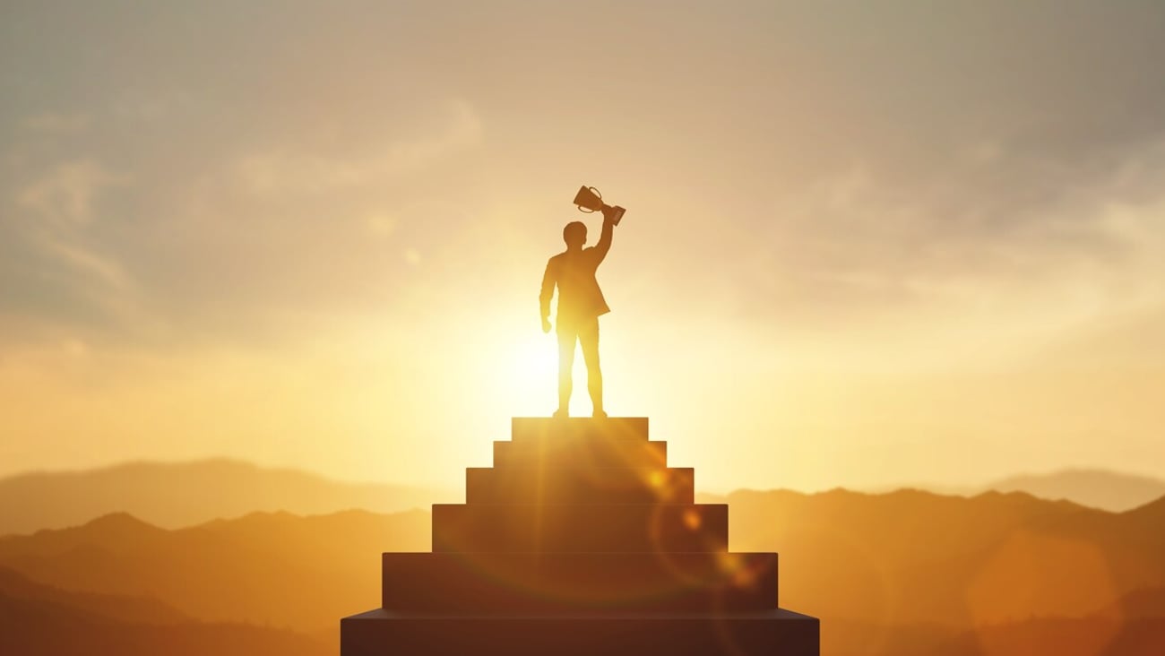 Silhouette of businessman holding a trophy on top staircase with light sunset. concept of a successful business or determination to lead the organization to success.; Shutterstock ID 2437023935