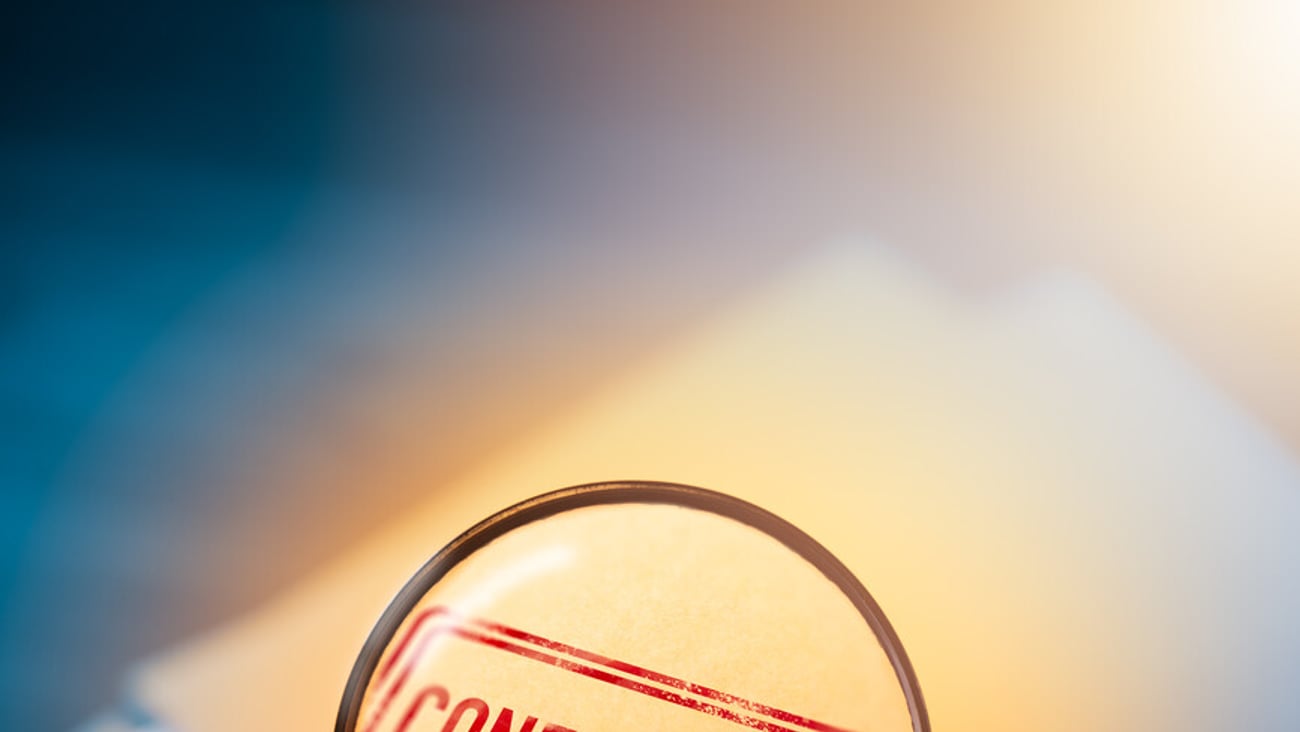 Private investigator holding a magnifying glass focusing on confidential envelopes; Shutterstock ID 1188564472