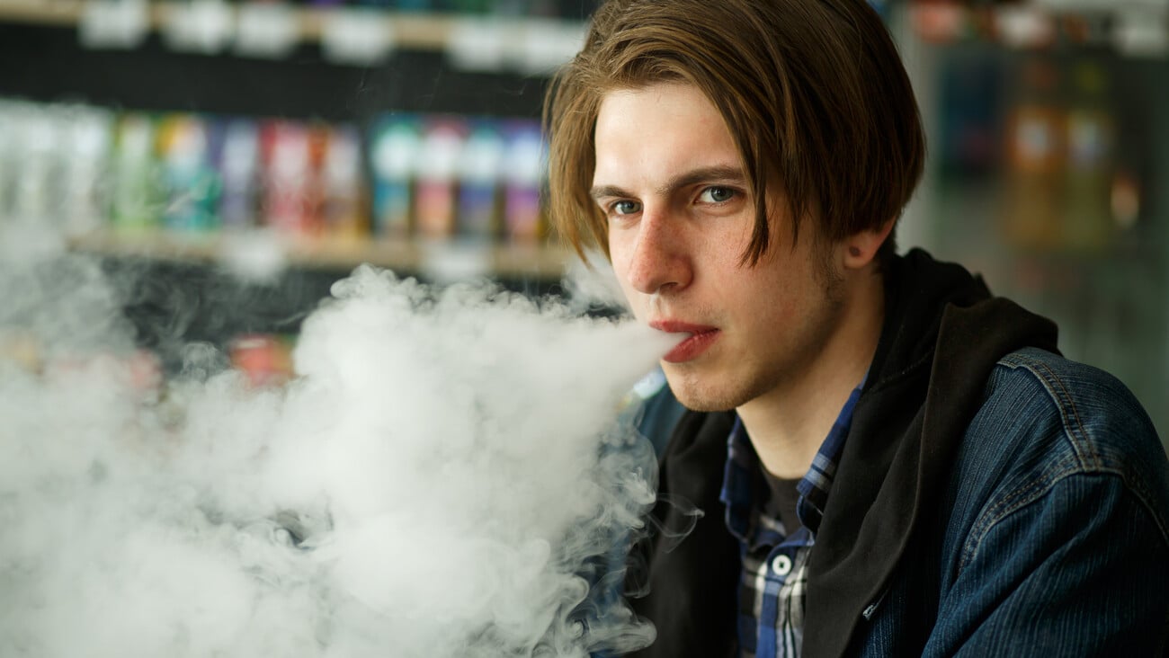 Vape teenager. Portrait of young handsome guy smoking an electronic cigarette in the vape bar. Bad habit that is harmful to health. Vaping activity. Close up.; Shutterstock ID 1400133746