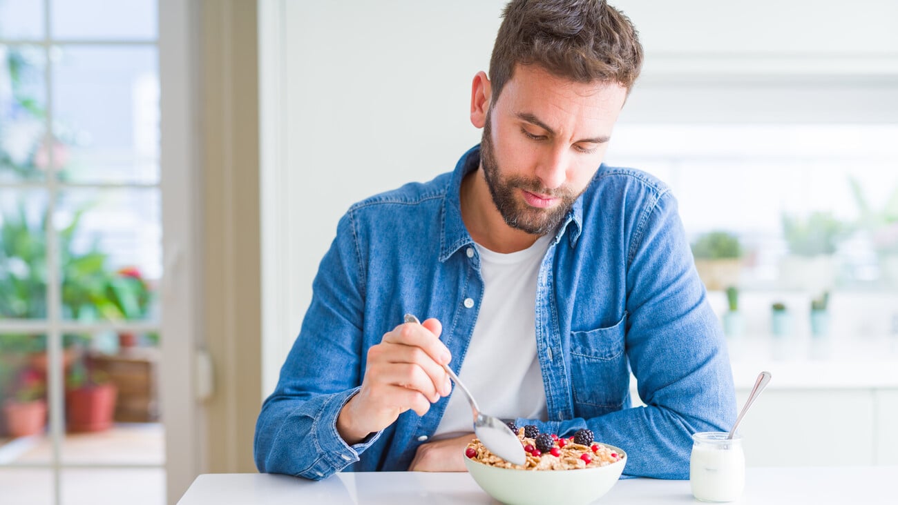 Handsome man having breakfast eating cereals at home and smiling; Shutterstock ID 1453256840