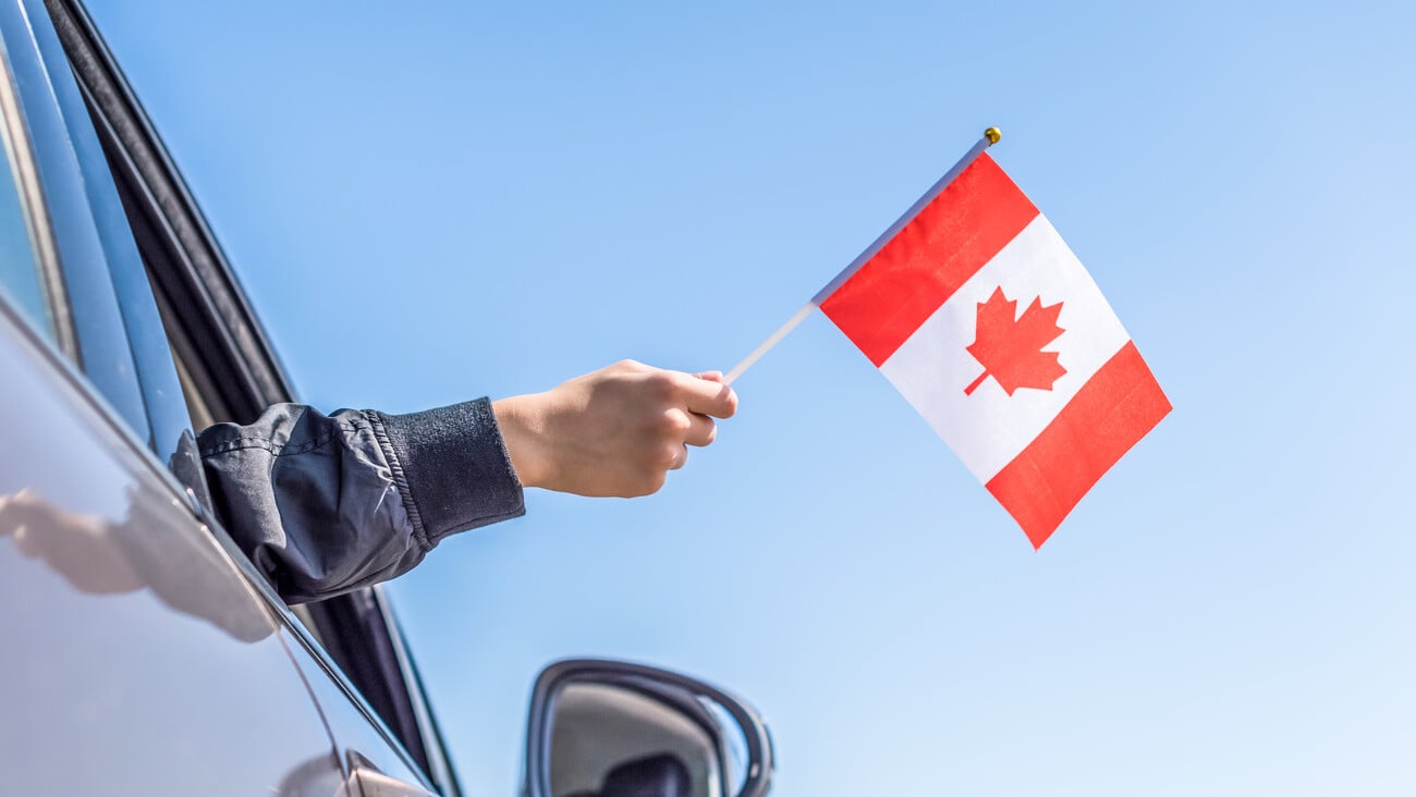 Boy holding Flag of Canada from the open car window on the sky background. USA.Concept ; Shutterstock ID 1477851167