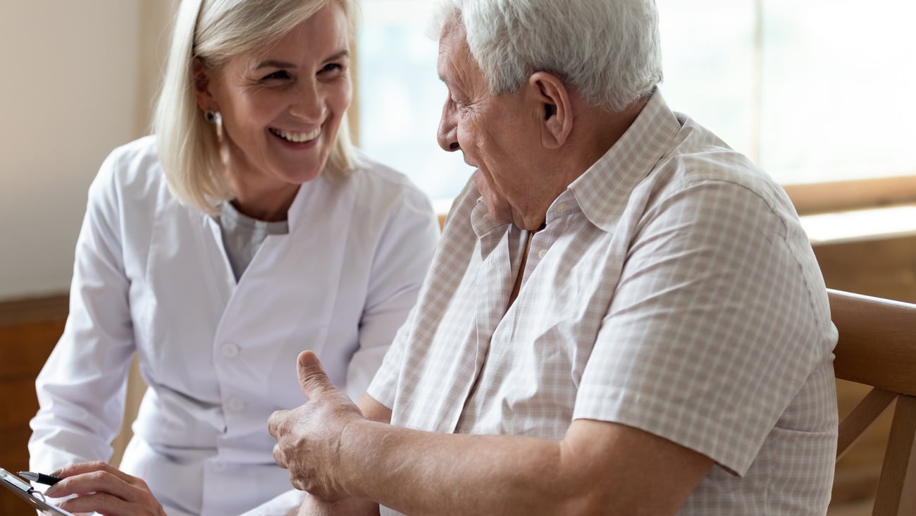 Elderly 80s man patient and middle-aged nurse medical worker holding clipboard writing personal information having pleasant warm conversation talk with clinic client nursing caregiving service concept; Shutterstock ID 1529466875