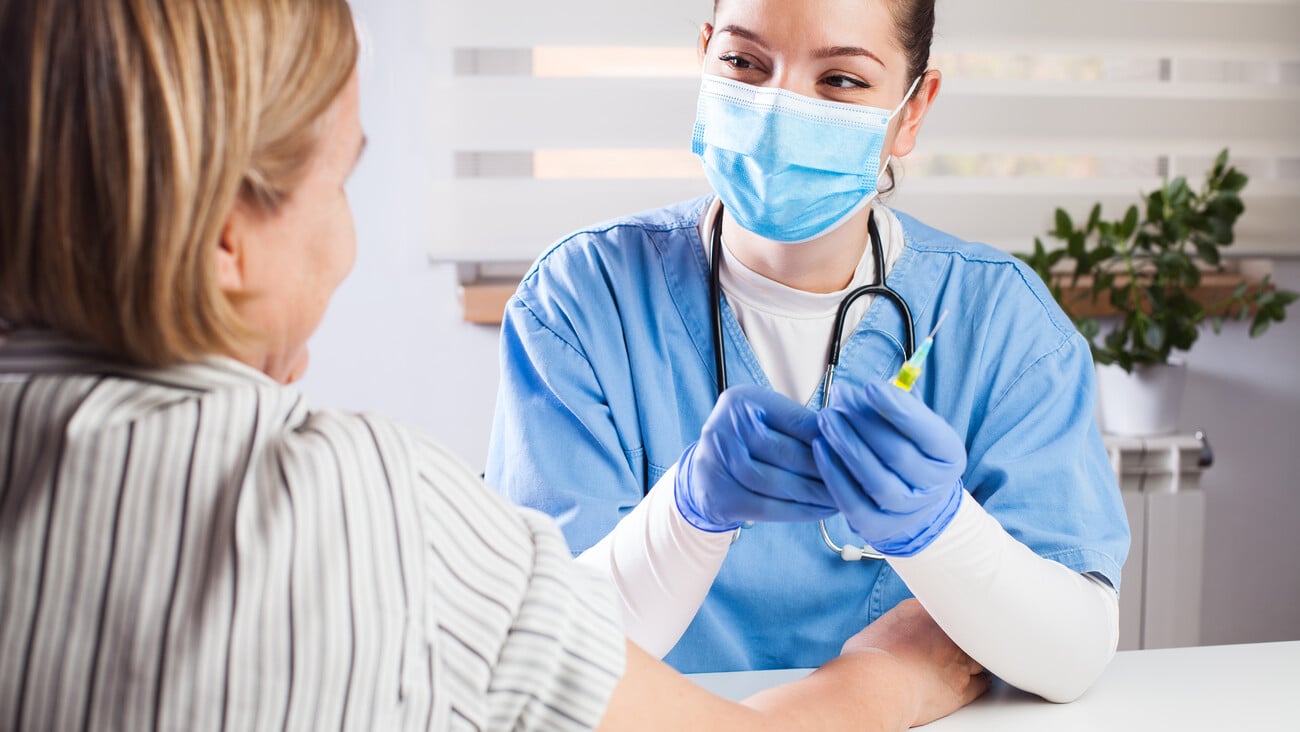 Young female caucasian GP doctor giving vaccine shot to elderly woman patient,General Practitioner holding syringe with yellow liquid,positive and relaxed,prevention,protection  immunization concept; Shutterstock ID 1735416938