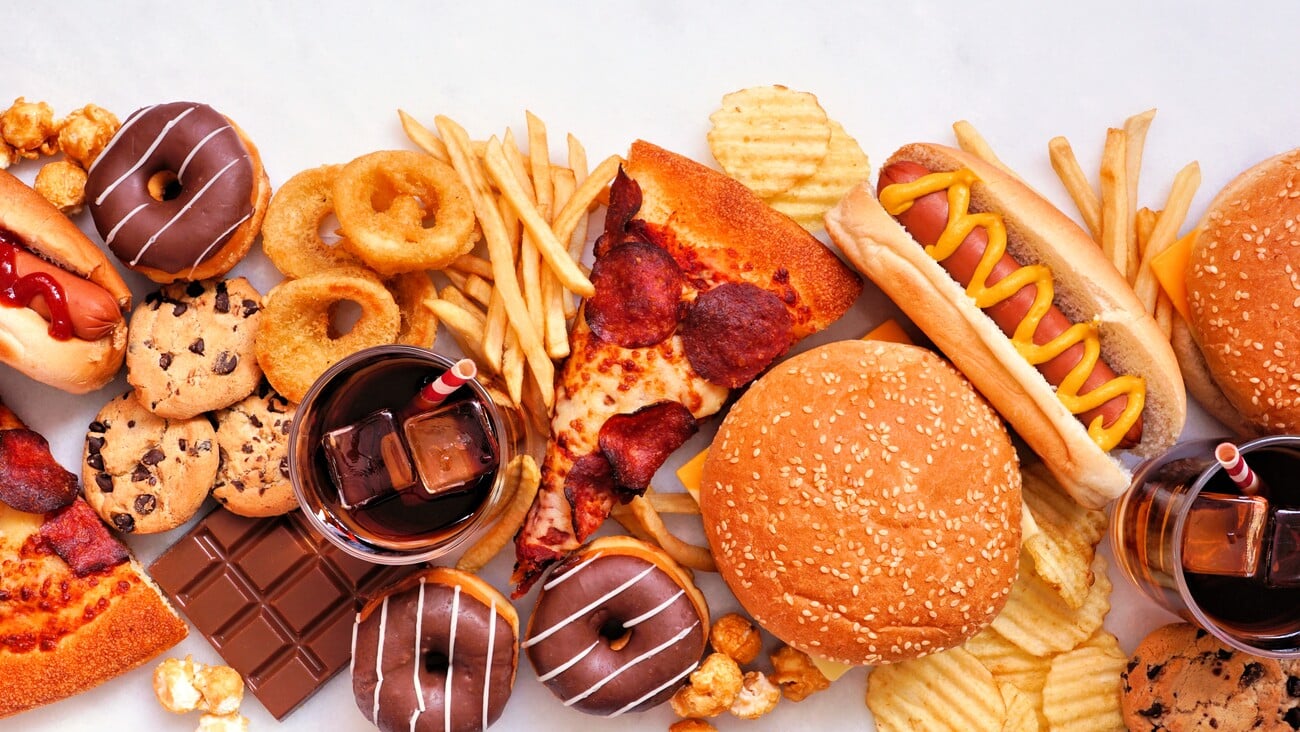 Junk food table scene scattered over a white marble background. Collection of take out and fast foods. Pizza, hamburgers, french fries, chips, hot dogs, sweets. Top view.; Shutterstock ID 2135456615