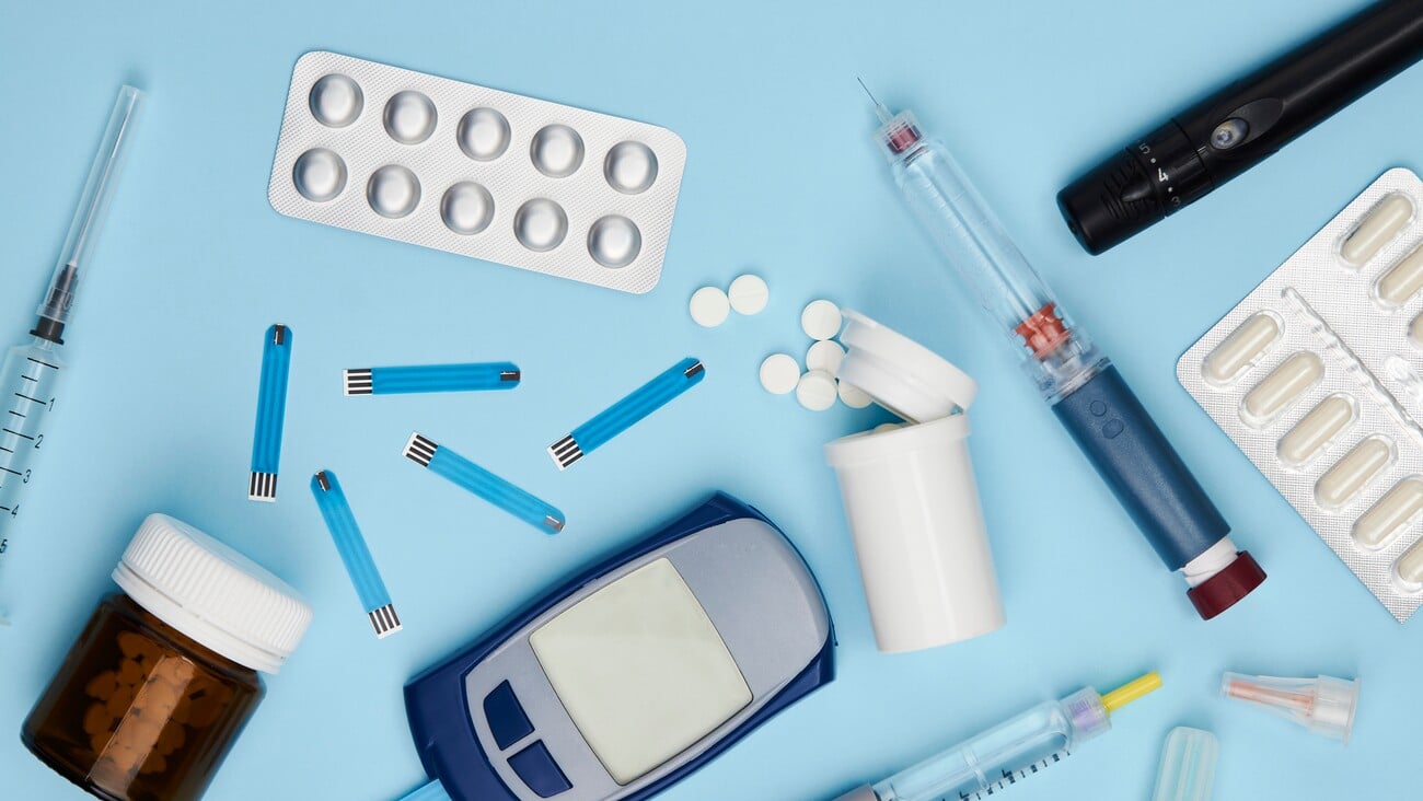 Diabetes concept with medical equipment on blue background with copy space. Glucose test glucometer, diabetic medicines, stripes and insulin syringe pen, top view; Shutterstock ID 2148124103