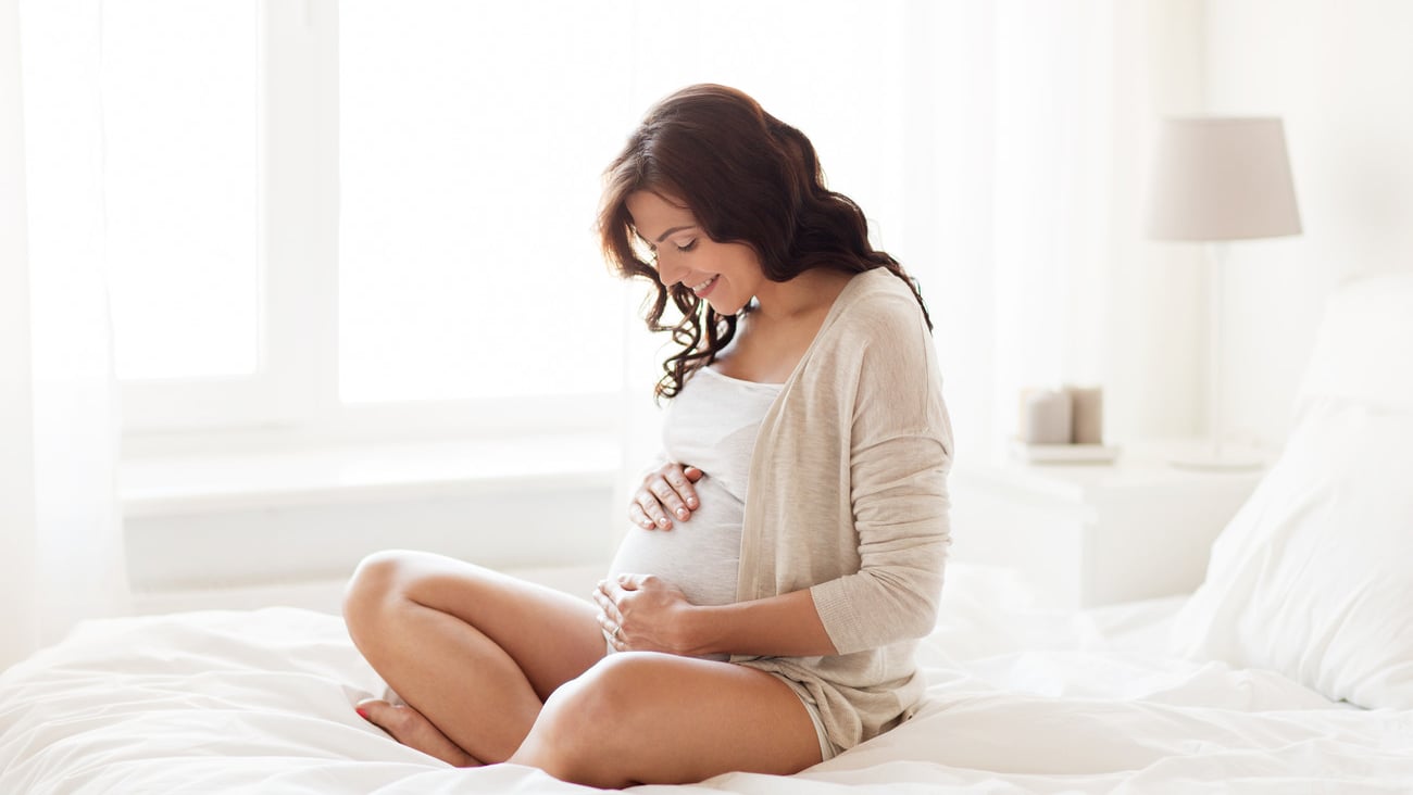 pregnancy, rest, people and expectation concept - happy pregnant woman sitting on bed and touching her belly at home; Shutterstock ID 476489323