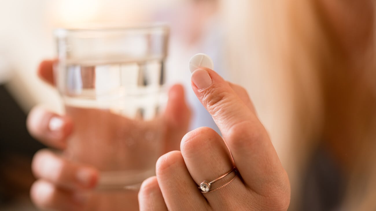 Close-up of the hands of a woman holding a pill and a glass of water; Shutterstock ID 567668200