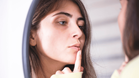 young woman checking out her cold sore in a mirror