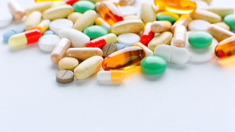 A selection of pills of different colours shapes and sizes on a white background.