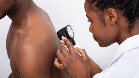 A young Black physician checks the back of a Black patient.