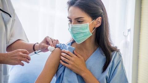Young woman in scrubs gets a vaccination from someone in a white coat