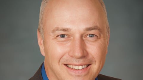 a man wearing a suit and tie smiling at the camera