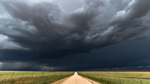 a large green field with clouds in the sky