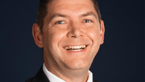 a man wearing a suit and tie smiling and looking at the camera