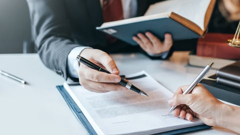 Two people point pens at a piece of paper sitting on a table.