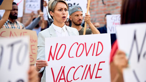 A woman without a mask holds a no covid vaccine poster at a protest