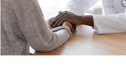 A Black physician holds hands with a Black patients; only hands are seen.