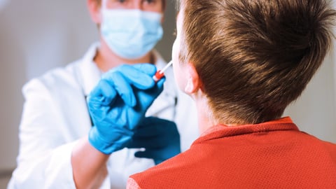 A child receives a COVID test nasal swab from a man in a lab coat wearing a mask