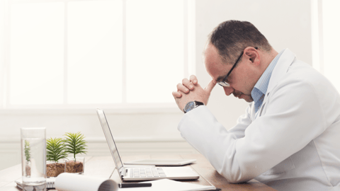 Pharmacist with head in hands, resting at laptop