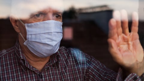 older man in mask waving at window