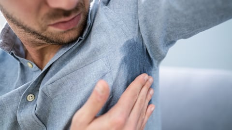 A man wearing a blu dress shirt looks at sweat that has soaked through the fabric at his armpit