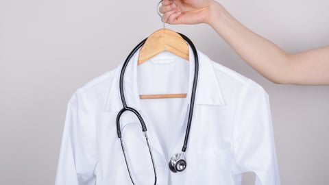 WOman's arm holding a lab coat on a hanger with a stethoscope